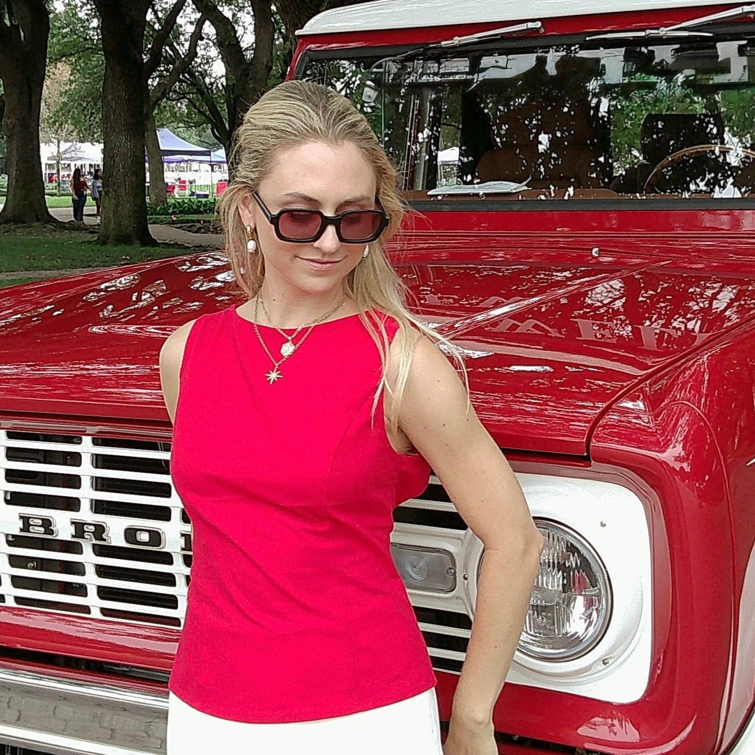 Woman in a pink top standing in front of a red truck with trees in the background