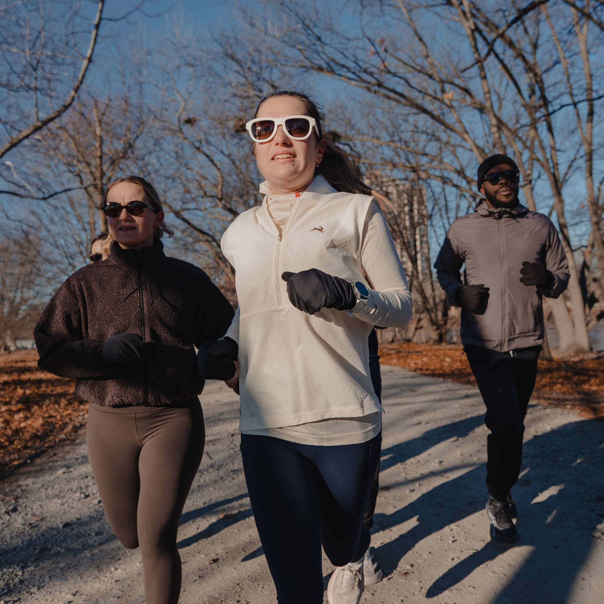 Three people running outdoors in sunglasses on a path with trees in the background