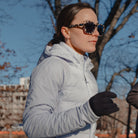 Person wearing a light gray puffer jacket and dark sunglasses outdoors.
