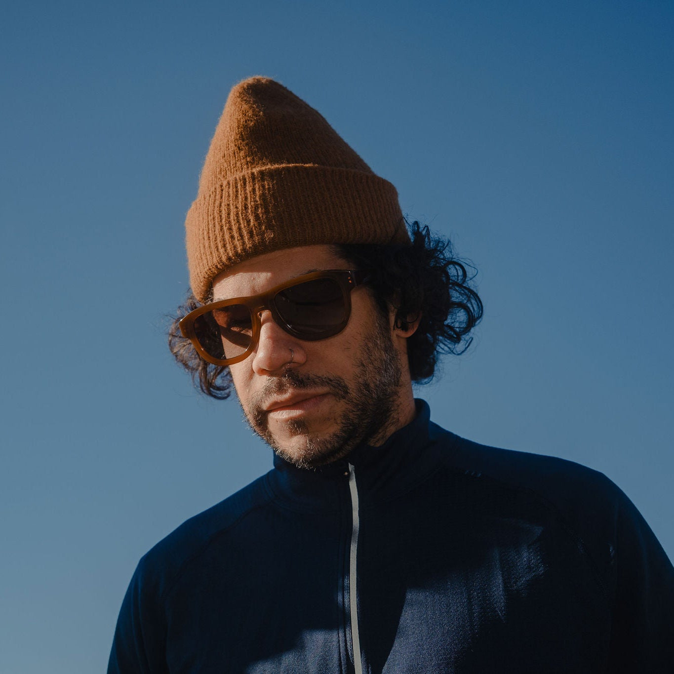 Man wearing a brown beanie and sunglasses against a clear blue sky