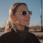Person wearing white sunglasses and a dark coat outdoors on a clear day