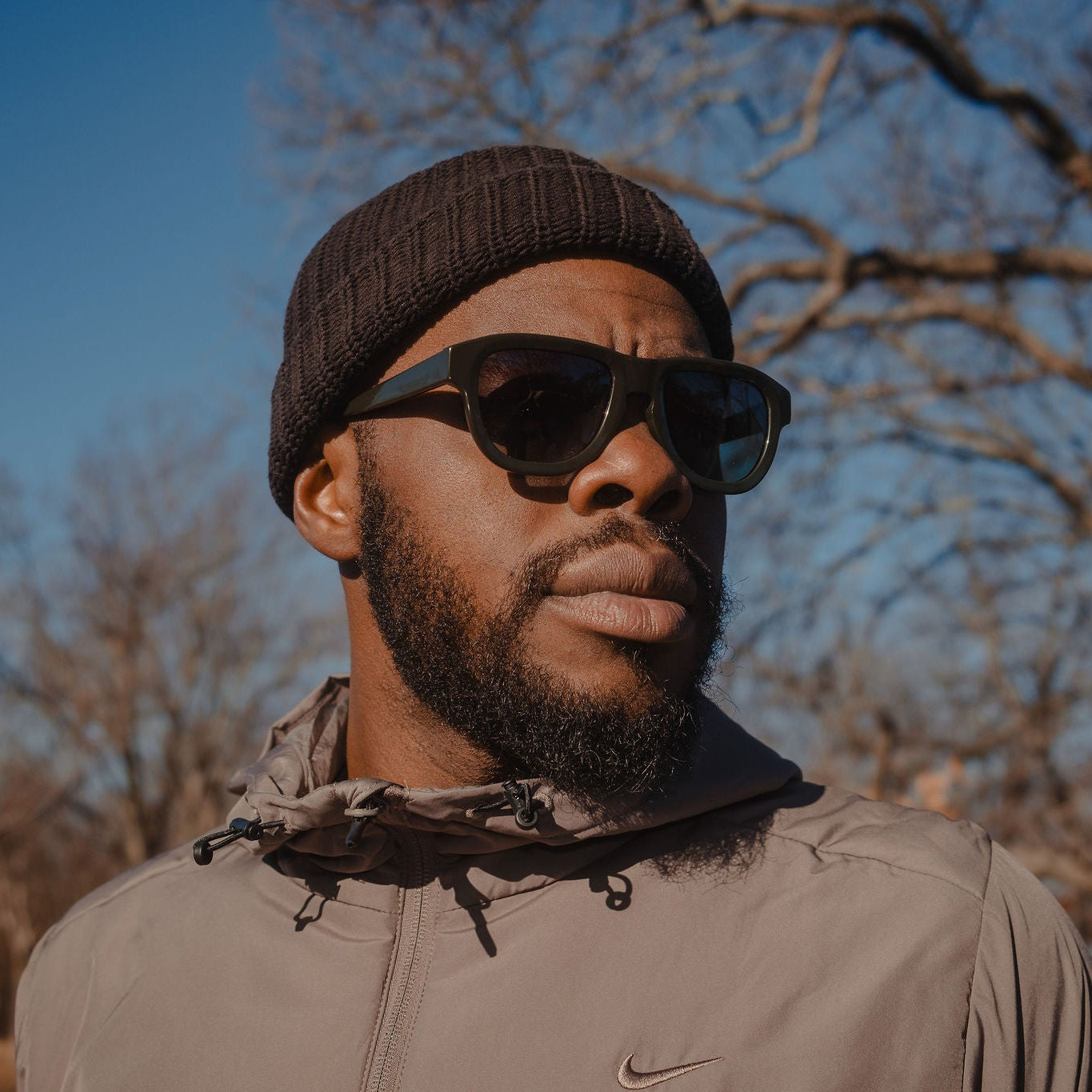 Man wearing sunglasses and a cap outdoors with trees in the background